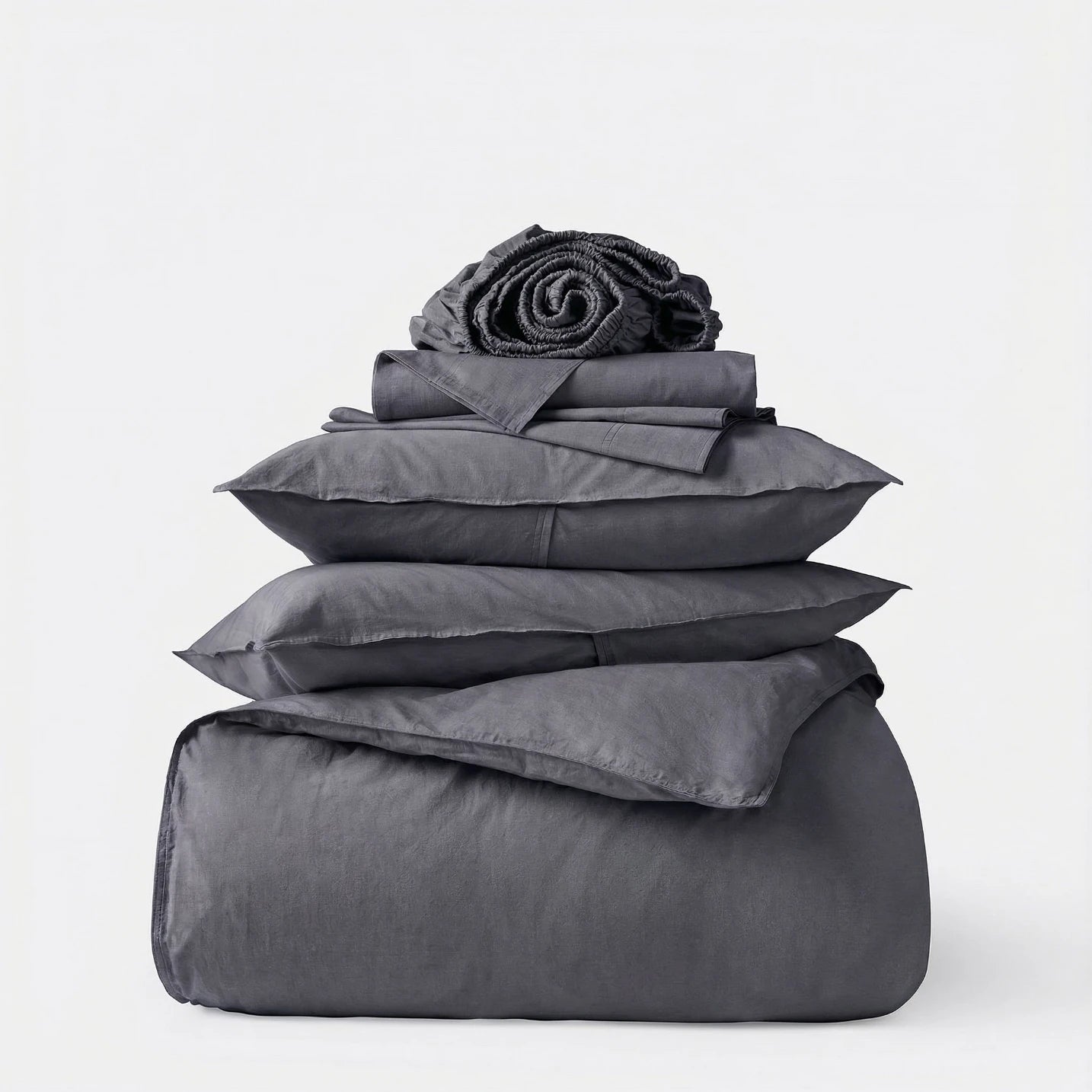 Stack of gray bedding including a duvet, comforter, and pillows on a white background