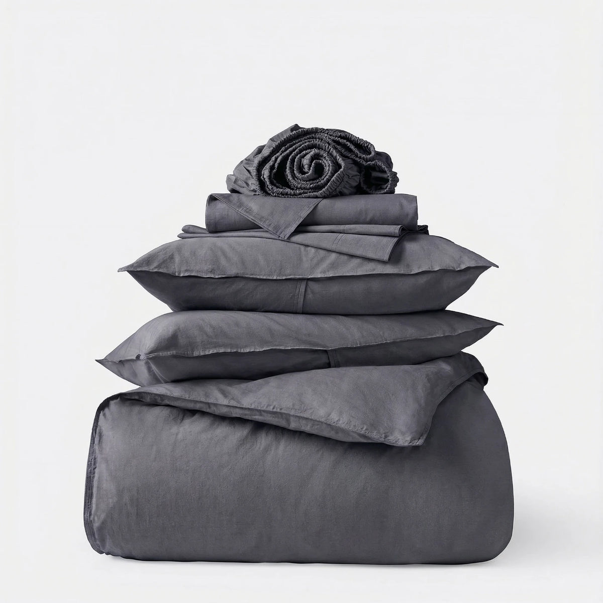 Stack of gray bedding including a duvet, comforter, and pillows on a white background