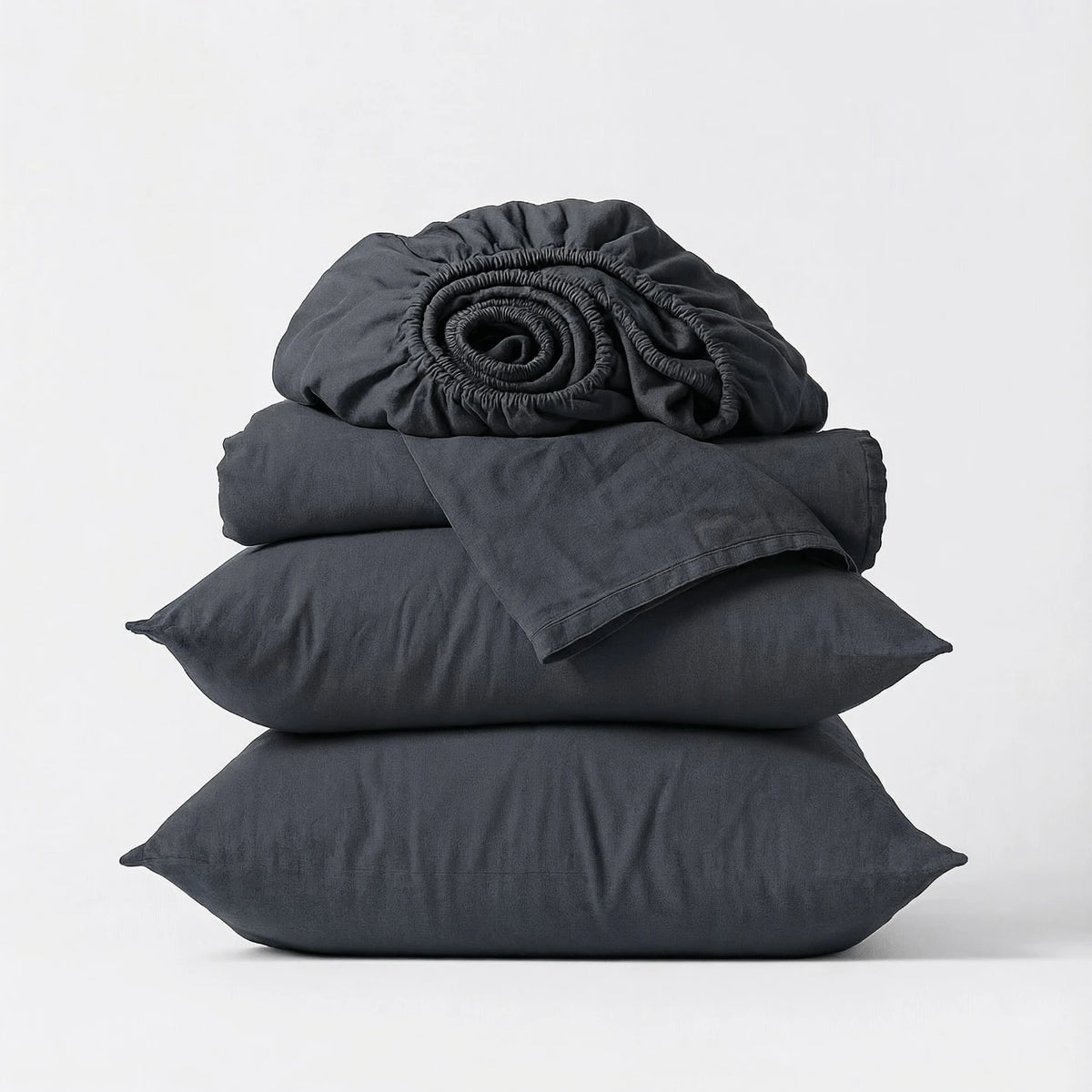 Stack of dark gray bedding including a fitted sheet, duvet cover, and pillows on a light gray background