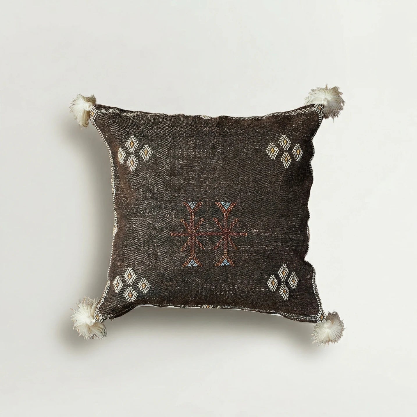 Decorative pillow with intricate patterns and tassels on a light gray background