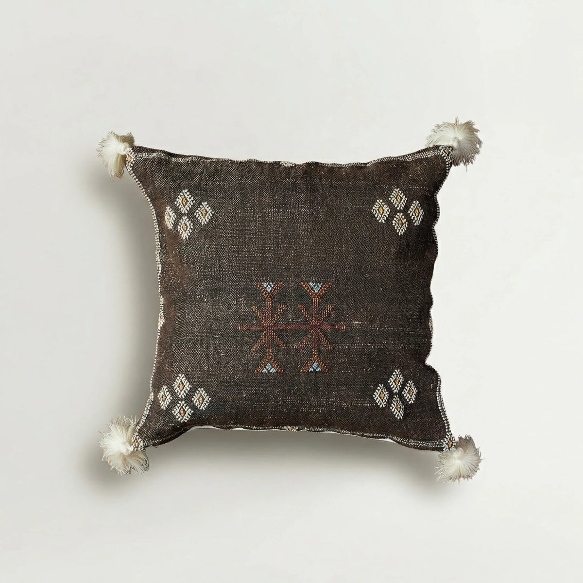 Decorative pillow with intricate patterns and tassels on a light gray background