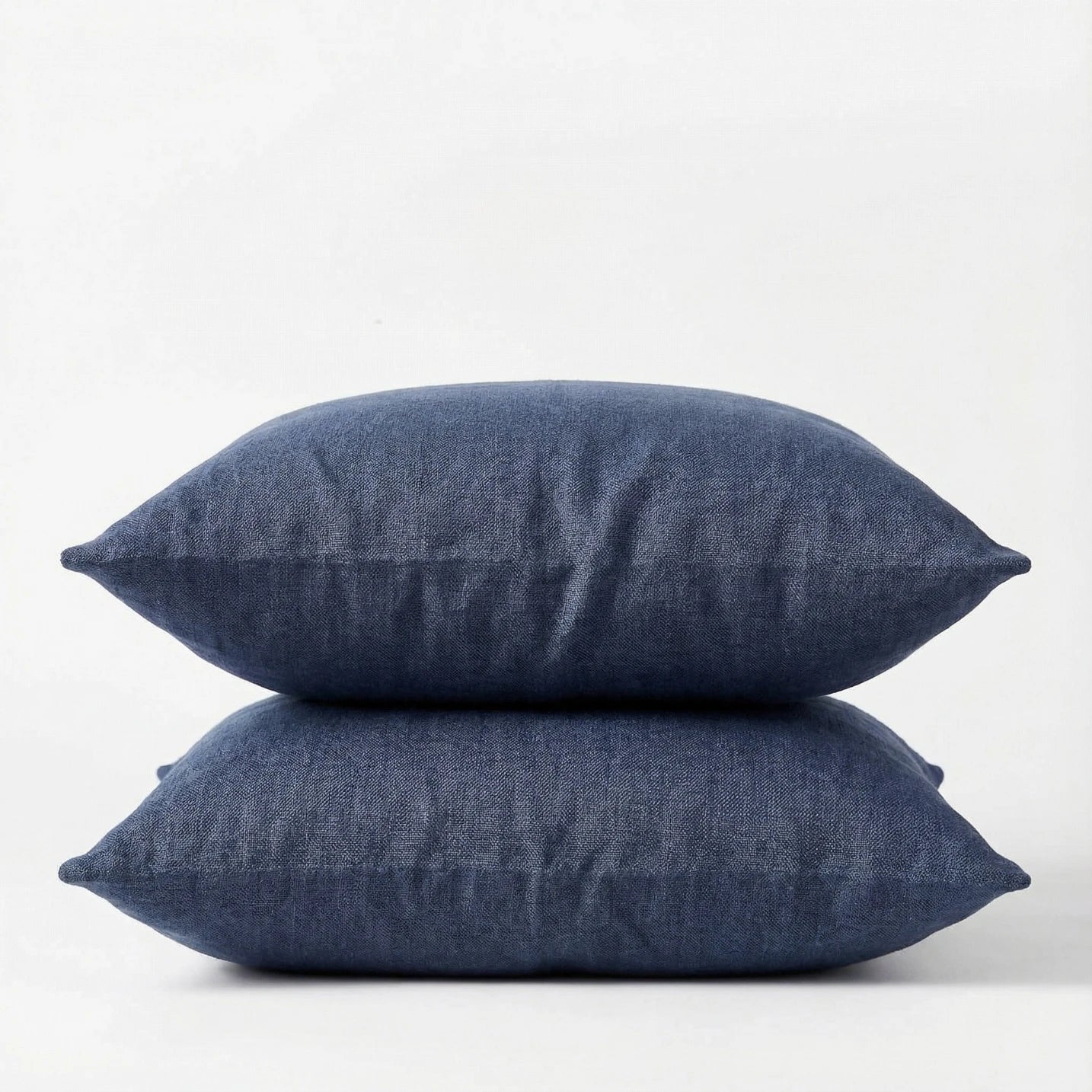 Two denim blue pillows stacked on a white background