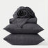 Stack of dark gray bedding including a fitted sheet, duvet cover, and two pillows on a white background.