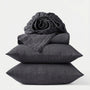Stack of dark gray bedding including a fitted sheet, duvet cover, and two pillows on a white background.