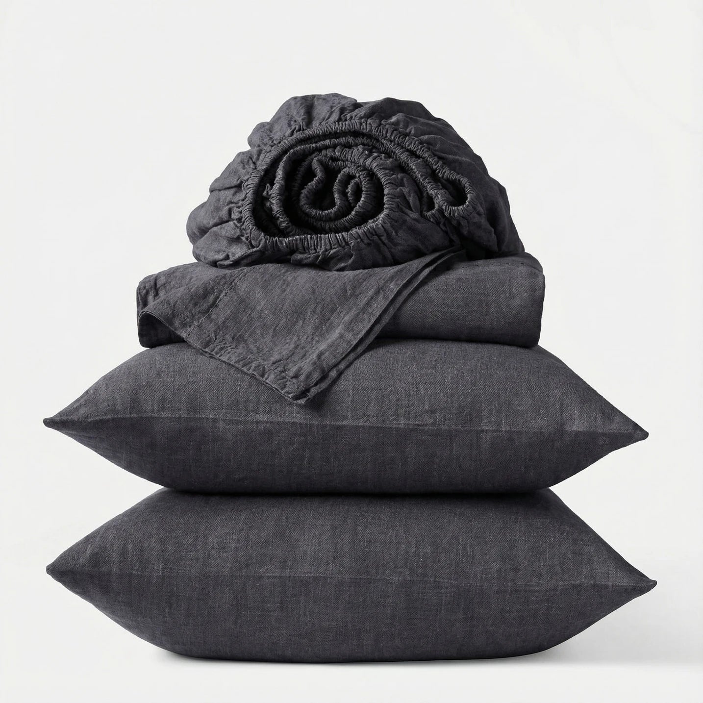Stack of dark gray bedding including a fitted sheet, duvet cover, and two pillows on a white background.