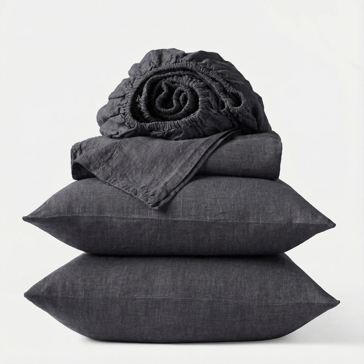 Stack of dark gray bedding including a fitted sheet, duvet cover, and two pillows on a white background.