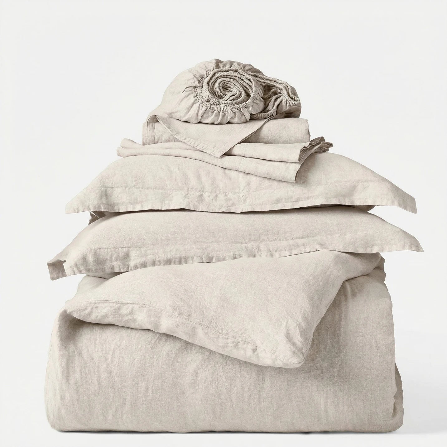 Stack of beige bedding including a duvet, pillowcases, and a blanket on a white background
